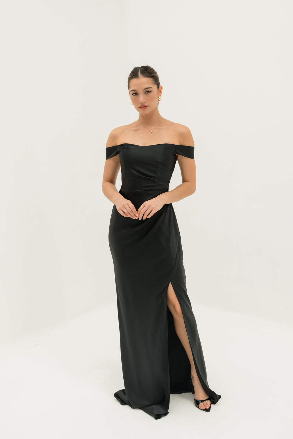 Woman wearing a black off-shoulder gown with a slit on a white background
